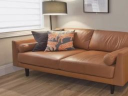 Brown leather sofa with decorative pillows and a lamp in a light-filled room.