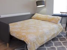 A neat sofa bed with a yellow patterned duvet cover and grey sofa frame.
