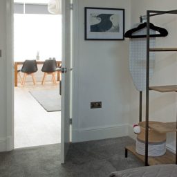 A modern interior with a view of a dining area, featuring a clothing rack and artwork.