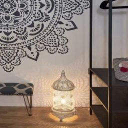 Decorative lantern casting intricate shadows on a patterned wall with a shelf.