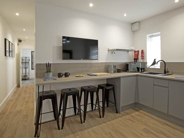 Modern kitchen with grey cabinets, a wooden countertop, and bar stools.
