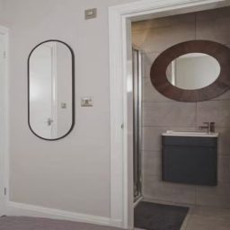 Neutral-toned bathroom with a oval mirror, modern sink, and shower area visible.