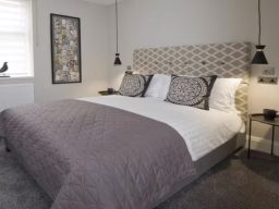 Modern bedroom featuring a large double bed with patterned headboard and stylish décor.