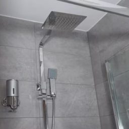 Modern shower with a square rain showerhead and silver fixtures in a tiled bathroom.