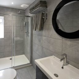 Modern bathroom with a walk-in shower, vanity unit, and circular mirror.