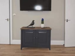 A dark cabinet with a wooden top, a bird statue, and a vase on display against a plain wall.