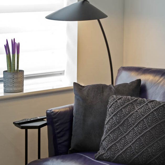 A modern purple armchair with cushions, a sleek floor lamp, and a potted plant nearby.