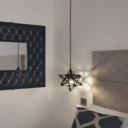 Star-shaped pendant light hanging next to a bed with a patterned cushion and decorative mirror.
