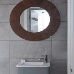 A minimalist bathroom featuring a round mirror above a grey sink unit.
