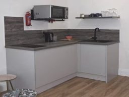 Modern kitchen with grey cabinets, a microwave, sink, and wooden flooring.