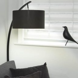 A modern black floor lamp next to a decorative bird figurine on a windowsill.