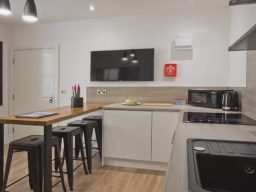 Modern kitchen with a wooden breakfast bar, black stools, and sleek appliances.