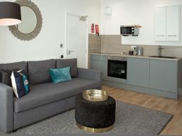 Modern open-plan living area with a grey sofa, coffee table, and kitchenette.