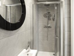 Modern bathroom featuring a shower cubicle, basin, and round mirror.