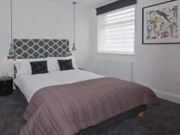 A modern bedroom featuring a double bed with a patterned headboard and artwork on the wall.