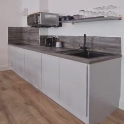 Modern kitchen with grey cabinets, a black sink, and a microwave above a countertop.