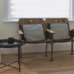 Two wooden chairs with cushions beside a small black table with a cup on it.