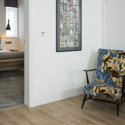 Colourful patterned armchair beside a doorway leading to a bedroom. Wall art in the background.