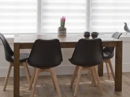 Modern wooden dining table with four black chairs and decorative plants.