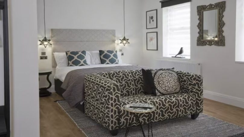 Modern bedroom featuring a patterned sofa, framed art, and pendant lighting.