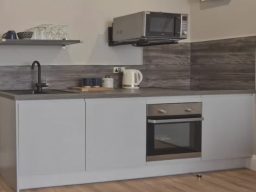 Modern kitchen with a grey cabinet, microwave, kettle, and oven on a sleek countertop.
